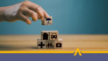 Ręka układająca drewniane klocki z ikonami domu, samochodu, zdrowia i rodziny