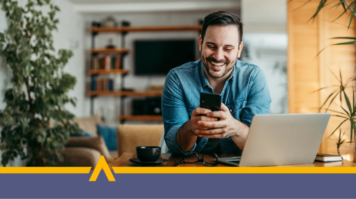 Uśmiechnięty mężczyzna korzystający z telefonu i laptopa w domowym biurze